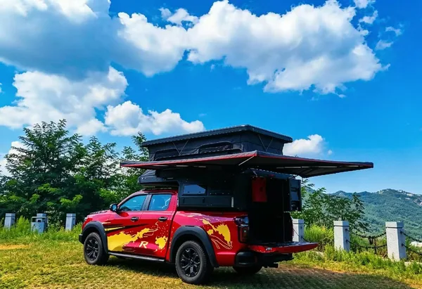 Red ute with the slide-on camper and awning open in the mountains