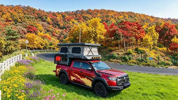 Red ute with a slide-on camper on a road through autumn hills