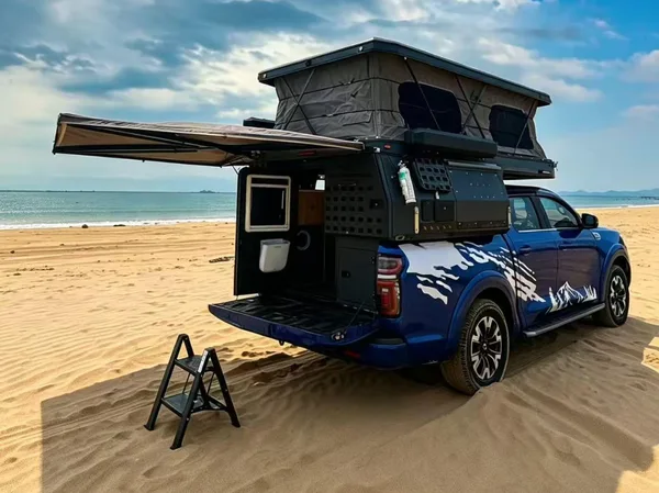 Blue ute with the slide-on camper open and awning out on a sandy beach