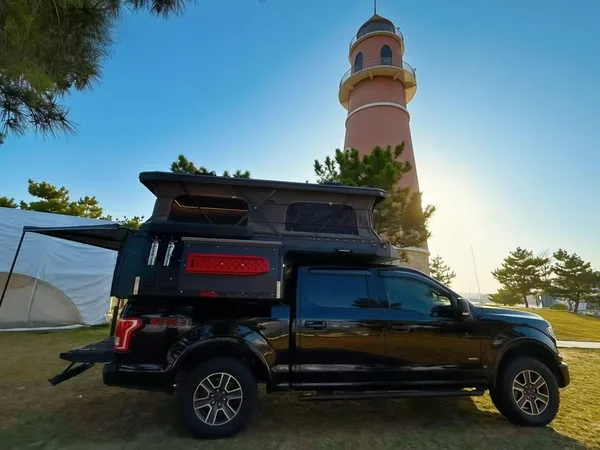 Black Ford F-150 with a slide-on camper beside a lighthouse