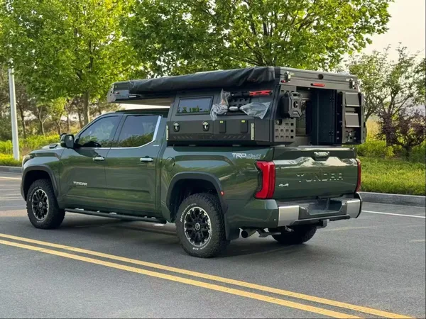 Green Toyota Tundra with a SUNHOMEE slide-on camper on a tree-lined road