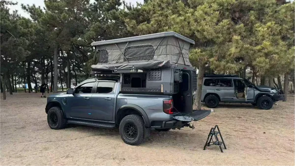 Grey ute with a slide-on camper at a pine-forest campsite, tailgate and step down