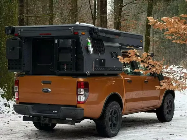 Orange Ford Ranger with a slide-on camper in a snowy forest, rear view