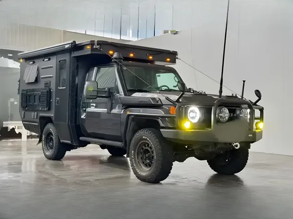 Black tray-mount camper on a Toyota Land Cruiser 79 with lights on