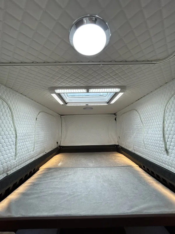 Empty camper interior before fit-out — insulated quilted walls, bed platform and roof hatch (DIY package)