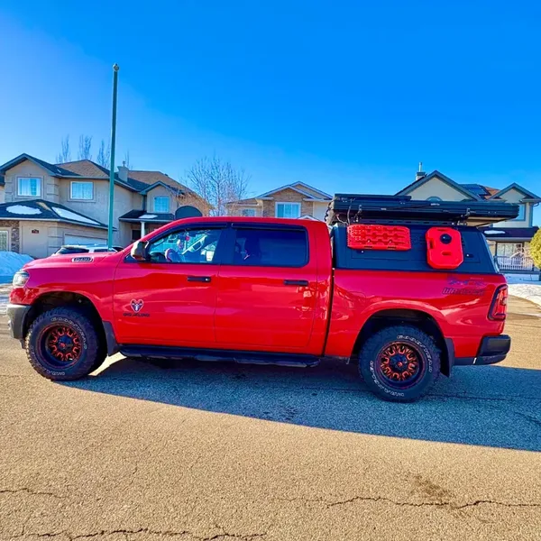 Side view of a red RAM pickup with a SUNHOMEE truck topper and roof rack